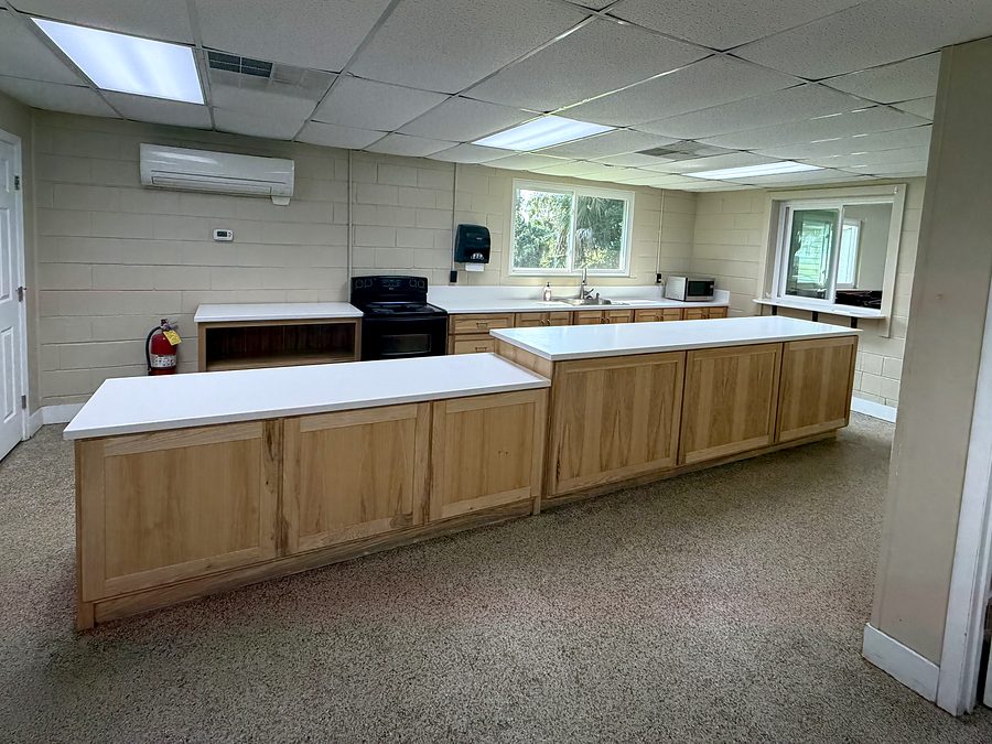 The club kitchen with electric range and oven, microwave, sink and long counters, and a serving window into the hall